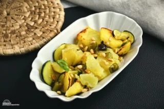 Warmer Kartoffel Zucchini Salat, eine optimale Beilage! 

Man bereitet Fisch im Ofen zu, macht einen Braten, die Hitze ist vorhanden, es duftet aus dem Ofen! Wir machen zur gleichen Zeit einen warmen Salat. Die Hitze muss genutzt werden und ein paar Röstaromen können auch dem Salat nicht schaden. So einfach geht die optimale Beilage zu Fleisch und Fisch. 

Gemüse aus dem Garten! 
Schon als Kind war mit der Salat bekannt. Ohne Nüsse oder Pinienkerne, die hatte meine Oma damals nicht. Es gab auch kein Olivenöl, der Salat wurde mit Speiseöl und etwas Essig mariniert. Warm war er trotzdem. Die Kartoffeln und die Zucchini stammten aus dem eigenen Gemüsegarten. Basilikum gab es auch nicht, Oma verwendete Petersilie oder ähnliche Kräuter.

Wir haben den Salat etwas in die moderne Zeit geholt, der Grundgedanke und das Basisrezept ist immer noch von Oma. Wir erinnern uns gerne an die Ratschläge und leben noch heute nach einigen Lebensweisheiten dieses besonderen Menschen. Oma wäre stolz auf uns. 

Der Ofen aus alter Zeit! 

Wir sind in der glücklichen Situation, einen alten Holzofen in der Küche zu haben. Ohne Strom, ohne Technik. Wir kochen gerne, vor allem im Winter, der Ofen macht zusätzlich ein schönes Raumklima. 

Es knistert, es duftet, es macht einfach Spaß und die Erinnerungen an längst vergangene Tage werden wach. Kocht man mit Emotion und Erinnerung, schmeckt das Essen gleich viel besser.